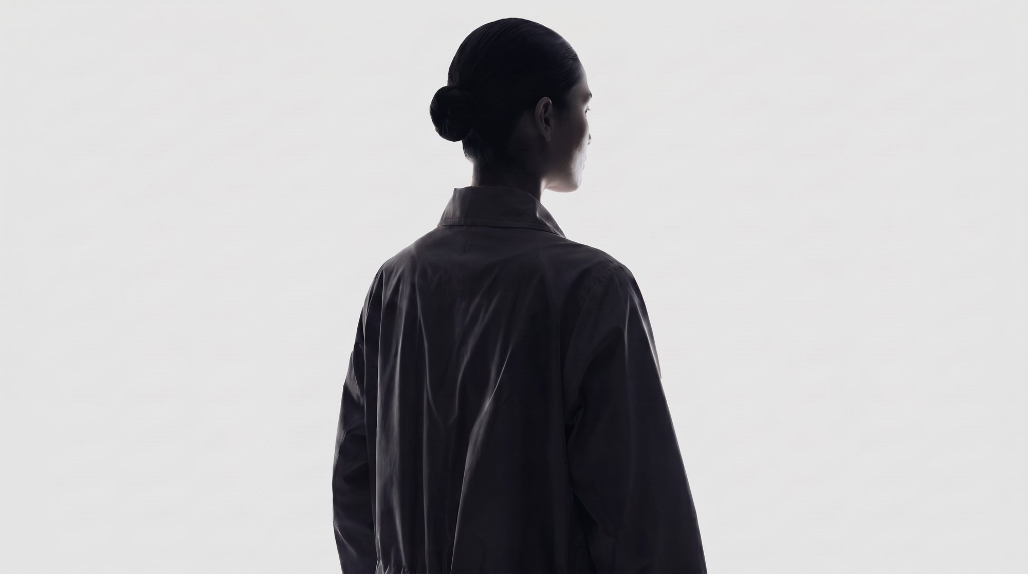 Model in a black jacket photographed from behind against a pale studio backdrop